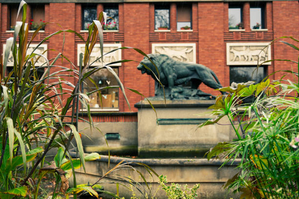 Paris, France â December 31, 2019: White lion statue in a European garden. A classic view with trees and a building in the background. Ideal for travel, culture, or history concepts.