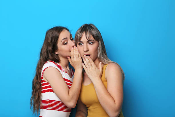 istock Two young woman whispering a secret on blue background 2193391183
