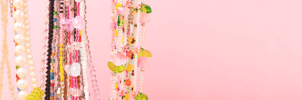 Close up on handmade beaded necklace made of white, blue and green beads on blue background surrounded by the beads and carnation flowers, DIY consept
