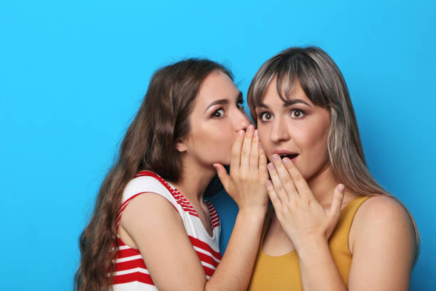 istock Two young woman whispering a secret on blue background 2193392168
