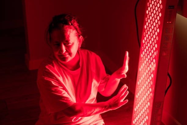 istock Elderly woman adjusting hands near red light therapy panel 2193393144