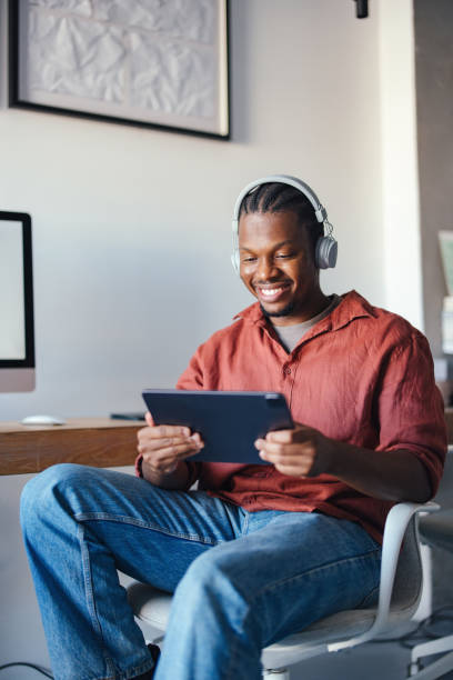 istock Smiling Man Using Tablet And Headphones in a Modern Office 2193393924