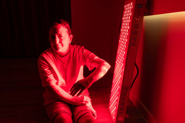 istock Elderly woman adjusting her arm position near a red light therapy panel 2193393930