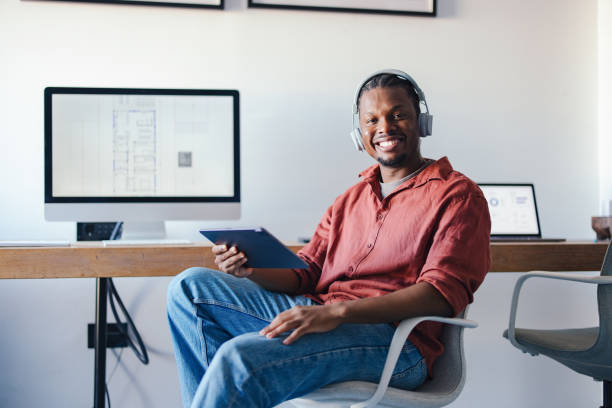 istock Smiling Young Professional at Desk Using Tablet and Headphones in a Creative Office 2193393956