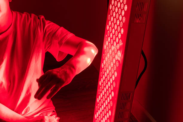istock Elderly woman sitting and positioning her arm for red light therapy 2193394043