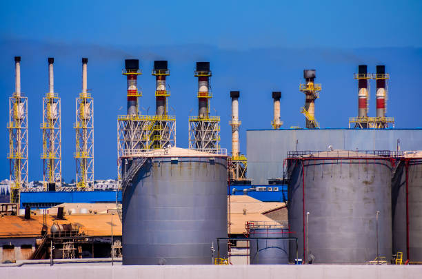 A large industrial plant with many tall tanks and pipes. The sky is clear and blue. Scene is industrial and somewhat ominous