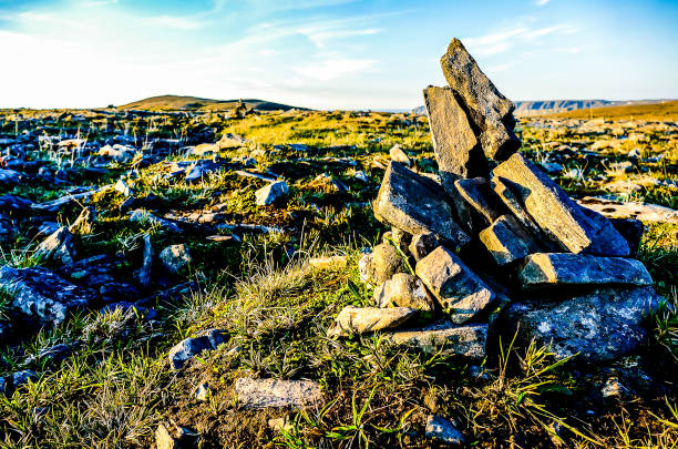 A rocky field with a large rock in the middle. The sky is blue and the sun is shining