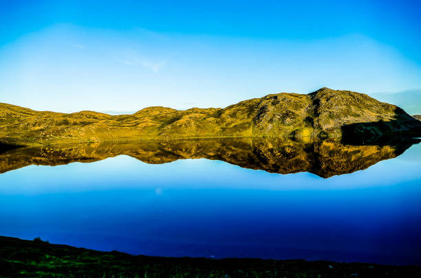 A beautiful lake with a mountain in the background. The water is calm and clear, reflecting the sky and the mountain. The scene is peaceful and serene, with the mountain providing a sense of grandeur