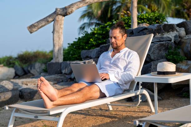 man working on computer on his beach vacation - nomaden stockfoto's en -beelden