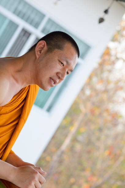 Candid portrait of thai monk outside of Wat Phrathat Doi Wiang Chai Mongkhon วัดพระธาตุดอยเวียงชัยมงคล – Temple Thai  Ping Khong, Chiang Dao District. Monk is head monk and running the temple inlcuding its restoration. Temple is more than 700 years old. Monk is talking to people and visitors of the temple and explaining history of place.