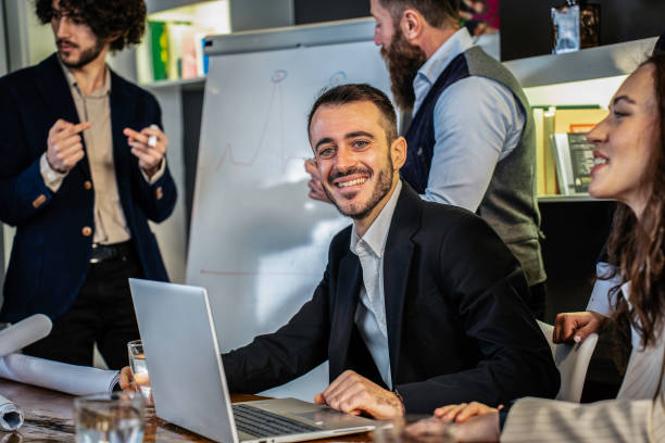 istock Young professional smiling confidently during a team meeting in a modern office. The image highlights collaboration and positive work dynamics in a corporate environment focused on success. 2193424106