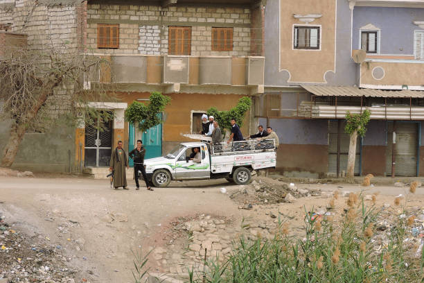 Nile, Egypt - March 28 2015 Modern Egyptians watch a passing cruise ship on the Nile. A group is in a Misubishi pickup truck. Two men are standing. One carries a Kalaschnikow