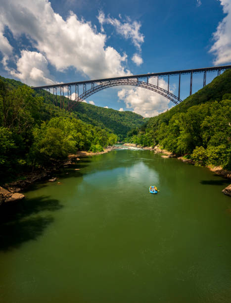 Rafters float towards the rapids under the high arched New River Gorge bridge in West Virginia