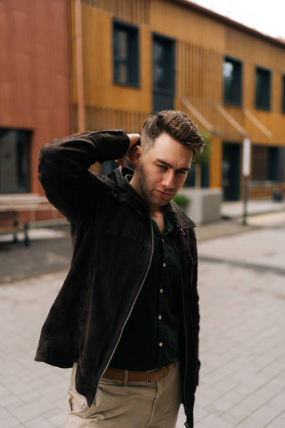 istock Stylish man looking at camera with confidence expression, adjusting hair while walking down street, radiating confidence and urban charm in trendy attire 2193433459