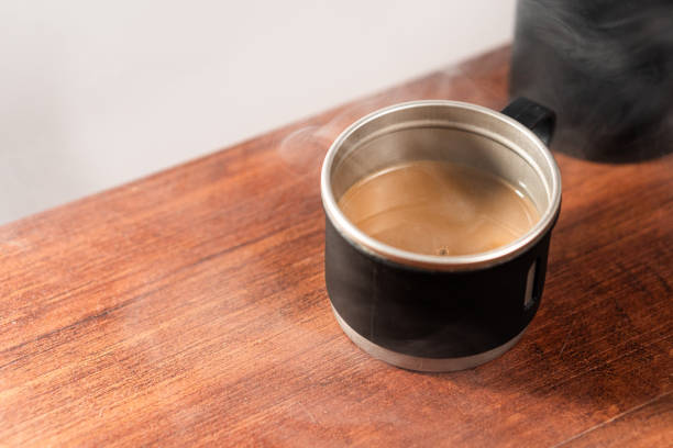 A steaming cup of coffee in a black mug on a wooden table.