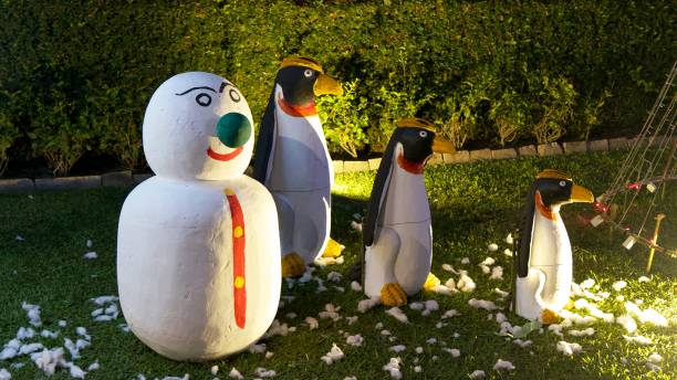 Illuminated penguin and snowman sculptures on a lawn during nighttime.