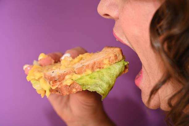 istock A woman is biting into a sandwich with melted cheese. 2193442722