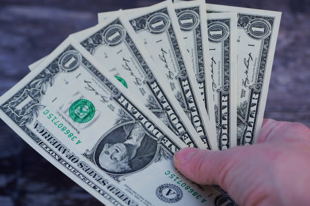 istock Hand holding multiple one dollar bills in a casual setting with dark background 2193457605