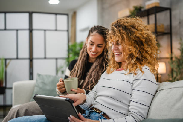 istock cheerful female friends sit on sofa and enjoy while use digital tablet 2193462845