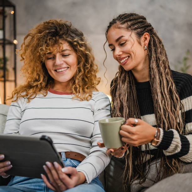 istock cheerful female friends sit on sofa and enjoy while use digital tablet 2193463049