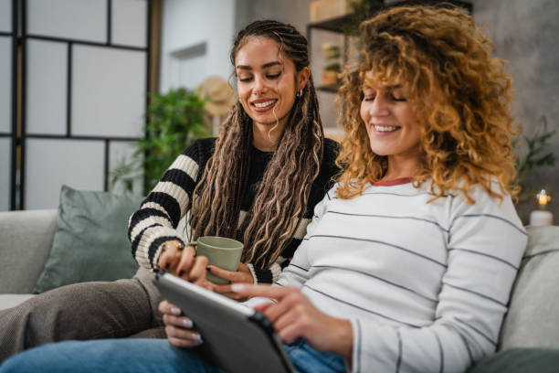 istock cheerful female friends sit on sofa and enjoy while use digital tablet 2193463837