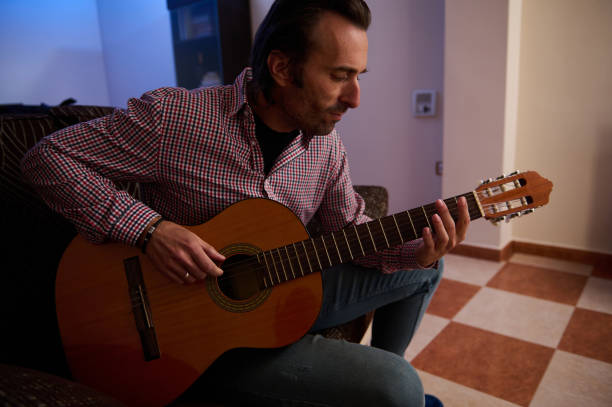 istock Man playing guitar sitting on a couch in a warm indoor setting 2193465146