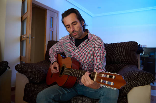 istock Man Playing Acoustic Guitar Sitting on a Couch at Home 2193465156