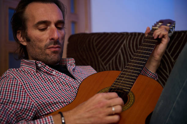 istock Man Relaxing While Playing an Acoustic Guitar on a Comfortable Couch 2193465161