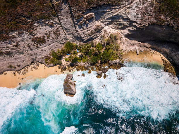istock Birds eye view of tropical waves crashing into a sandy beach and vertical cliffs 2193471283