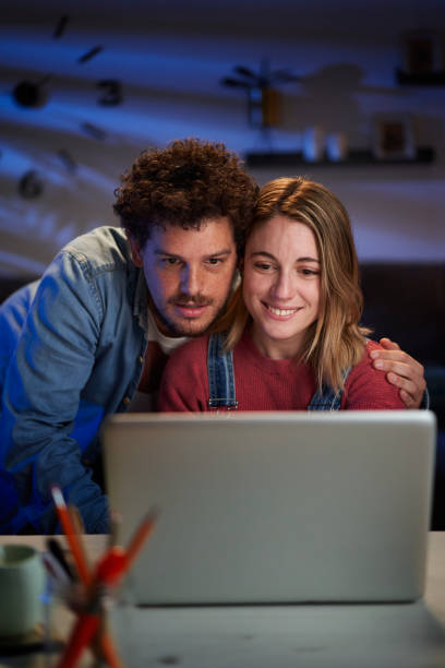 istock Vertical two happy young Caucasian people together looking at computer sitting desk at night home. 2193473583