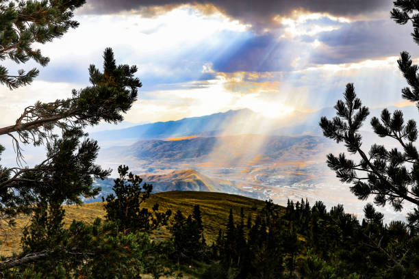 A dramatic capture of Lone Peak, with rain clouds parting to reveal bursts of sunlight over the rugged mountain terrain. A testament to the unpredictable beauty of high-altitude weather.