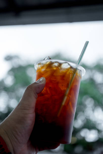 Hand holding ice black tea in takeaway glass. Thai drink