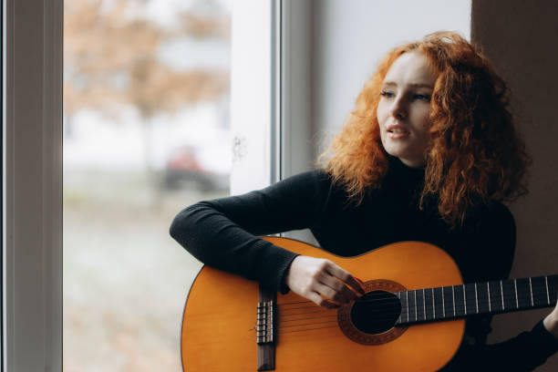 A redheaded girl plays guitar by the window