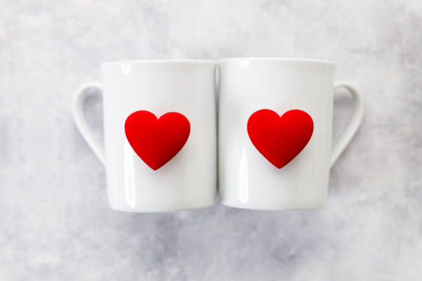 Cups of coffee or tea for two with red heart shaped ornament on white marble background. Valentineâs day and love concept.