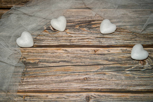 From above heart shaped white marble stones while decorated with thin transparent veil around and placed on wooden surface in light