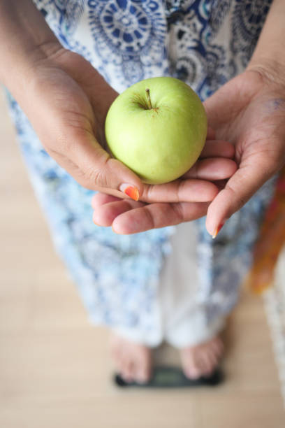 A person gently holds a vibrant, shiny green apple with a lively floral dress in the background