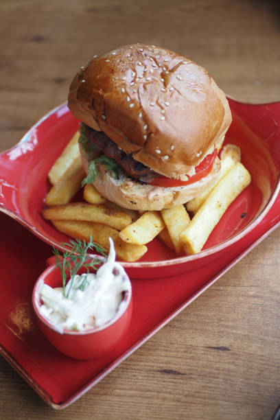 A delicious burger with crispy fries and dipping sauce, elegantly arranged on a red plate