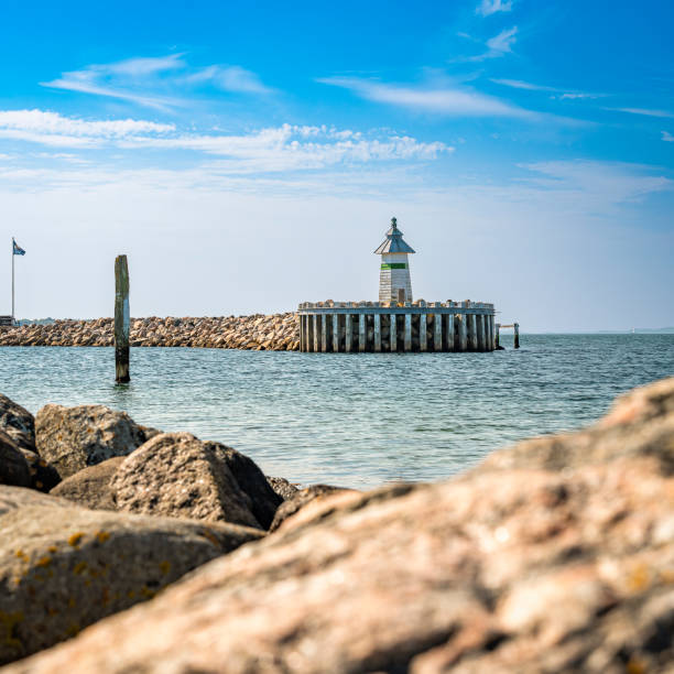 View of the West Mole Head light in the harbor entrance of Ebeltoft, in the foreground out of focus stones of the coastline, 1:1 format