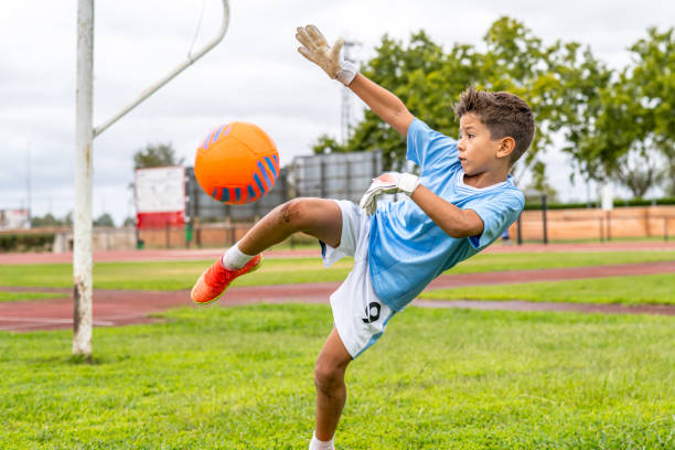 istock Young soccer goalkeeper training, wearing protective gloves while powerfully kicking orange and blue ball during intense practice session 2193504483