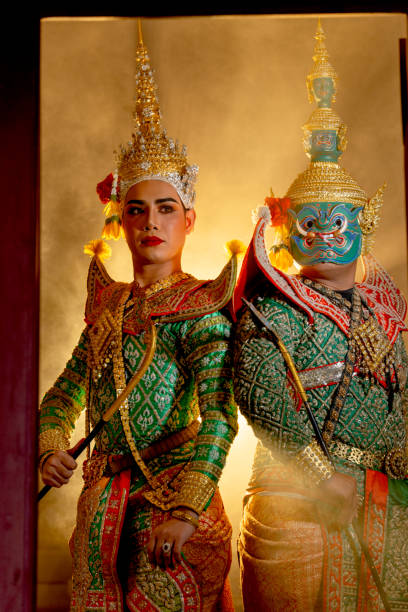 istock Vertical image two charactors of Khon mask costume stand with backs leaning against each other and giant mask stand in right side at door frame with beam light in the back. 2193511910