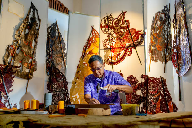 istock Front view Asian senior man wear glasses use hammer and chisel to create grand shadow play craft and he concentrate to work in area of workplace with several products are place around workplace area. 2193511981