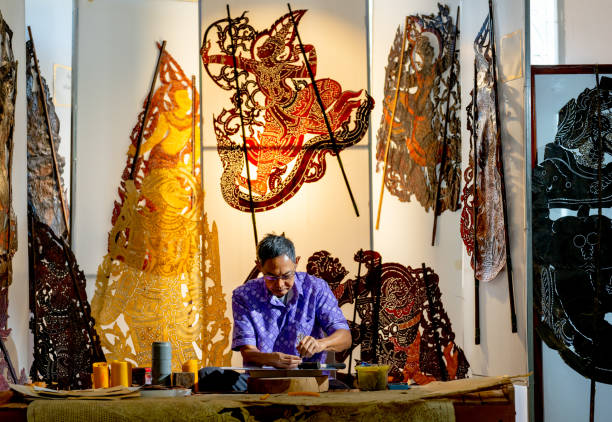 istock Front view Asian senior man wear glasses use hammer and chisel to create grand shadow play craft and he concentrate to work in area of workplace with several products are place around workplace area. 2193511984