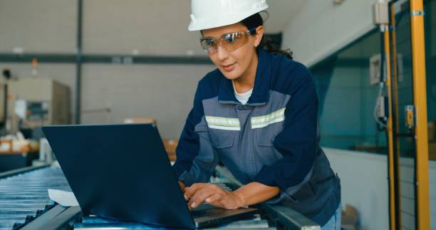 istock Young female engineer wearing hardhat uses laptop to analyze data and manage operations in factory. Robotic Industrial Factory. 2193512192