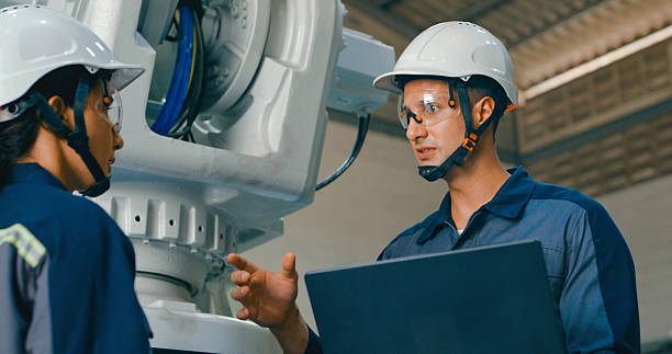 istock Closeup of Two young engineers, one using laptop and the other handheld device, collaborate in factory to manage robotic arm. Robotic Industrial Factory. 2193512240