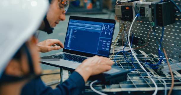 Two young engineer in factory programs robotic equipment using laptop, focusing on automation and precision technology. Robotic Industrial Factory.