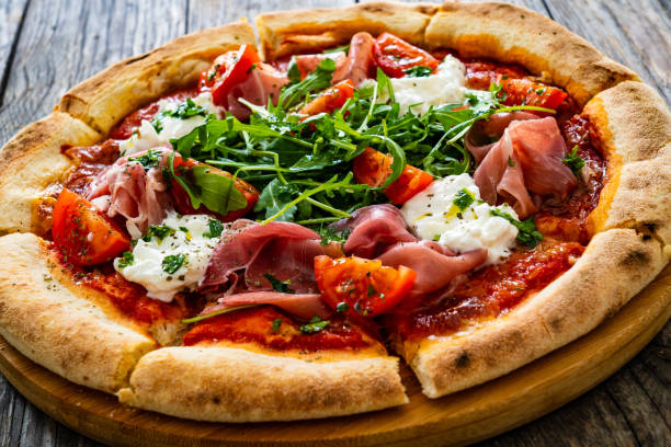 istock Pizza prosciutto - cured ham, white mushrooms, arugula and cheese on wooden table 2193513125