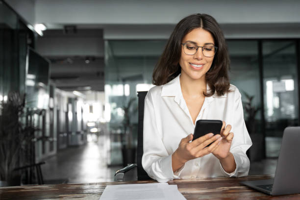 istock Middle aged Hispanic business manager ceo using cell phone mobile app, laptop. Smiling Latin or Indian mature woman businesswoman holding smartphone sit in office working online on gadget, copy space. 2193514285