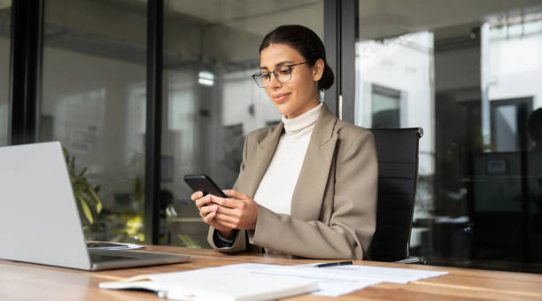 istock Middle aged Hispanic business manager ceo using cell phone mobile app, laptop. Smiling Latin or Indian mature woman businesswoman holding smartphone sit in office working online on gadget, copy space. 2193514320