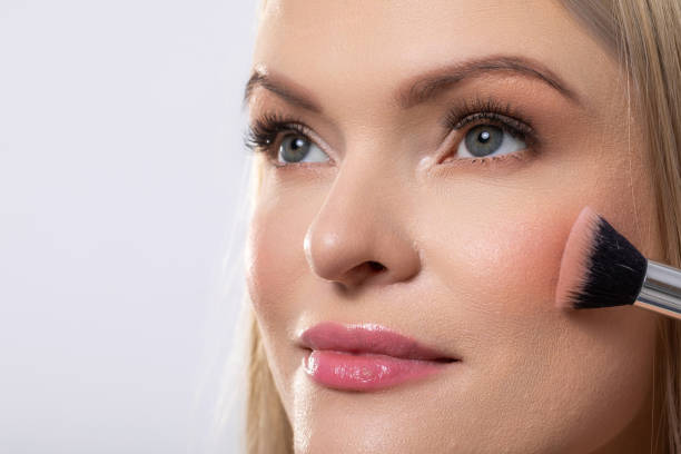Closeup of a woman putting soft blush on her cheeks, highlighting beauty and makeup artistry intricacies