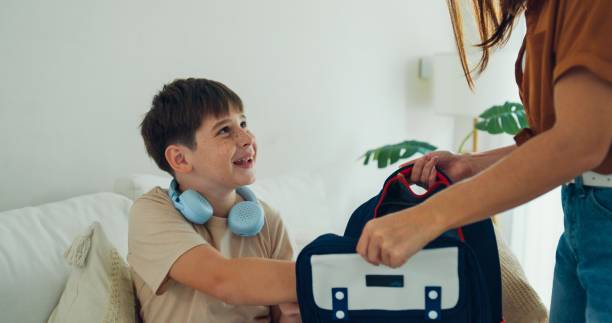 istock Young mother helps her son prepare his backpack in the living room for school, emphasizing a supportive and caring family moment. Back to school. 2193515655